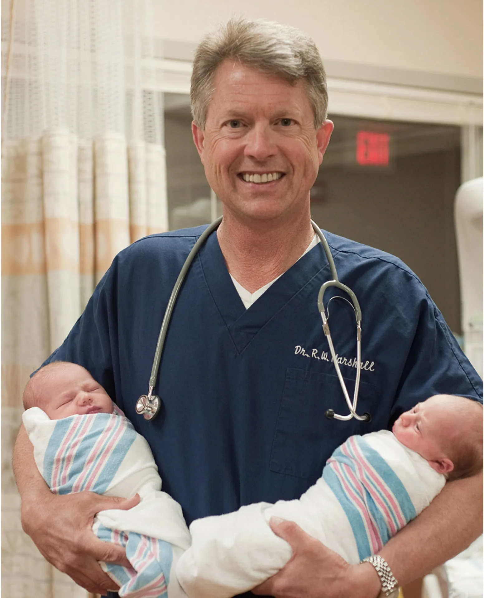 Dr. Roger W. Marshall in scrubs, holding two newborns.
