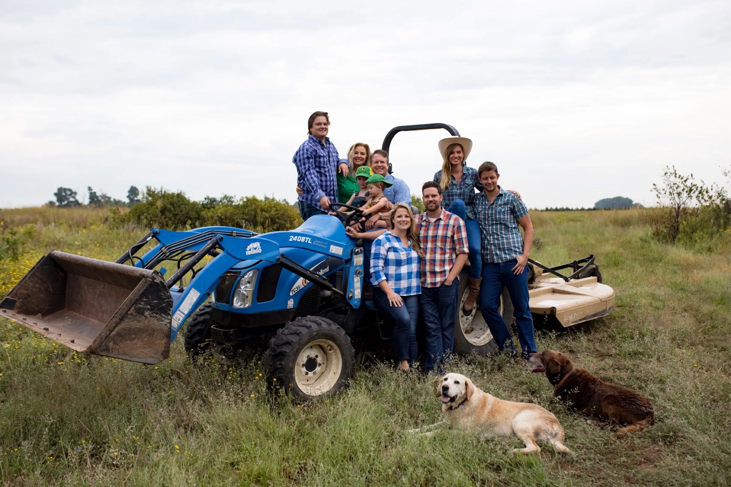 Some of the Marshall family with their dogs around a blue tractor in a Kansas hayfield.